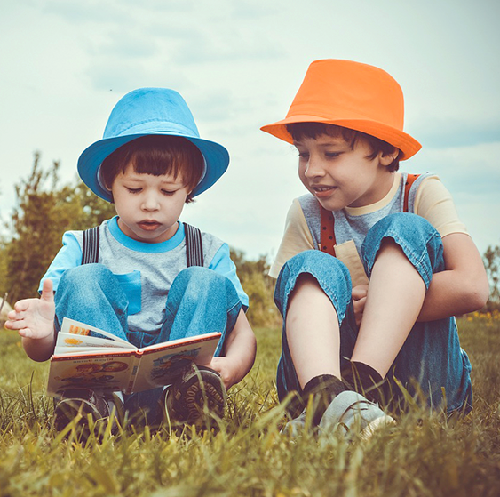 2 boys sitting, reading a book in a field